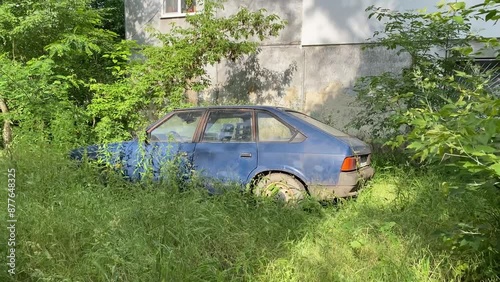 Old blue soviet car left near the house wall in bushes