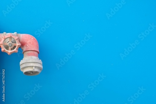 A photo of red grey small water pipe wth a small wheel in a background of a blue wall
