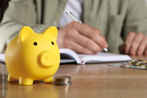 Man at wooden table, focus on yellow piggy bank. Space for text