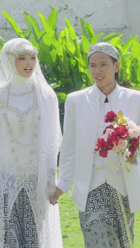 Young Asian Newlyweds In Traditional Wedding Outfit Walking Together While Holding Flower Bouquet and Marriage Books