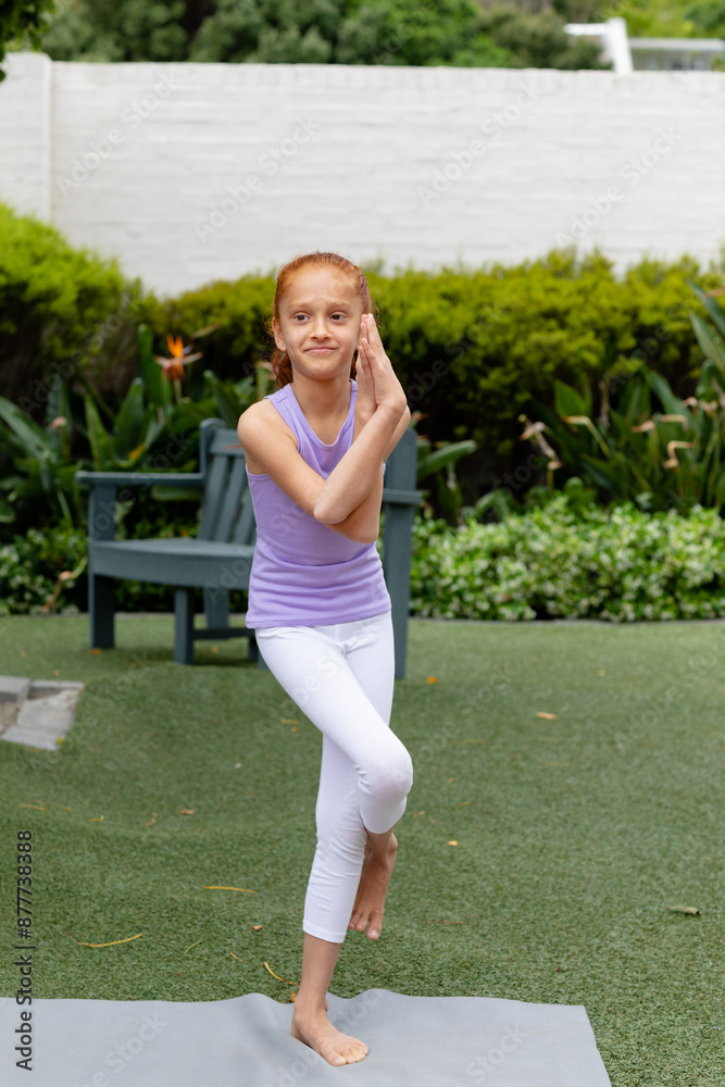 Fototapeta premium Vertical of happy biracial girl standing on one leg in garden, practicing yoga, with copy space