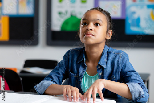 Blind biracial schoolgirl sitting at desk in class reading braille, with copy space