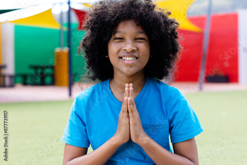 Portrait of smiling biracial schoolgirl practicing yoga meditation in schoolyard, with copy space photo