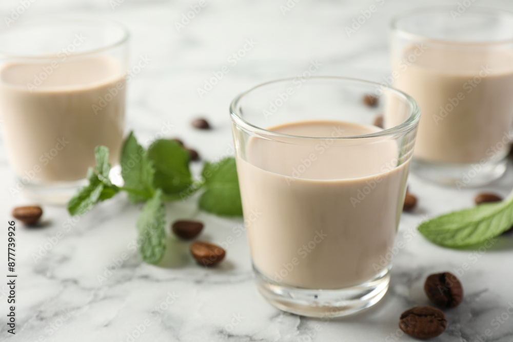 Coffee cream liqueur in glasses, mint and beans on white marble table, closeup Coffee cream liqueur in glasses, mint and beans on white marble table, closeup