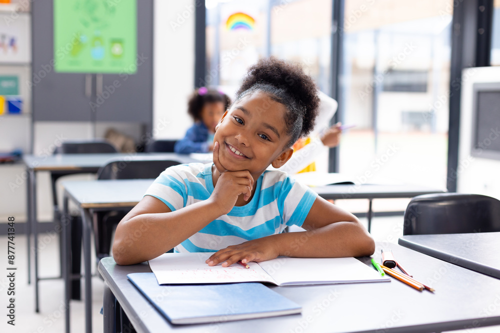 Portrait of happy african american schoolgirl sitting at desk in school classroom Portrait of happy african american schoolgirl sitting at desk in school classroom