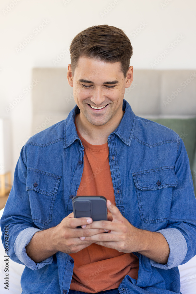 Smiling man using smartphone while sitting on bed in casual outfit Smiling man using smartphone while sitting on bed in casual outfit