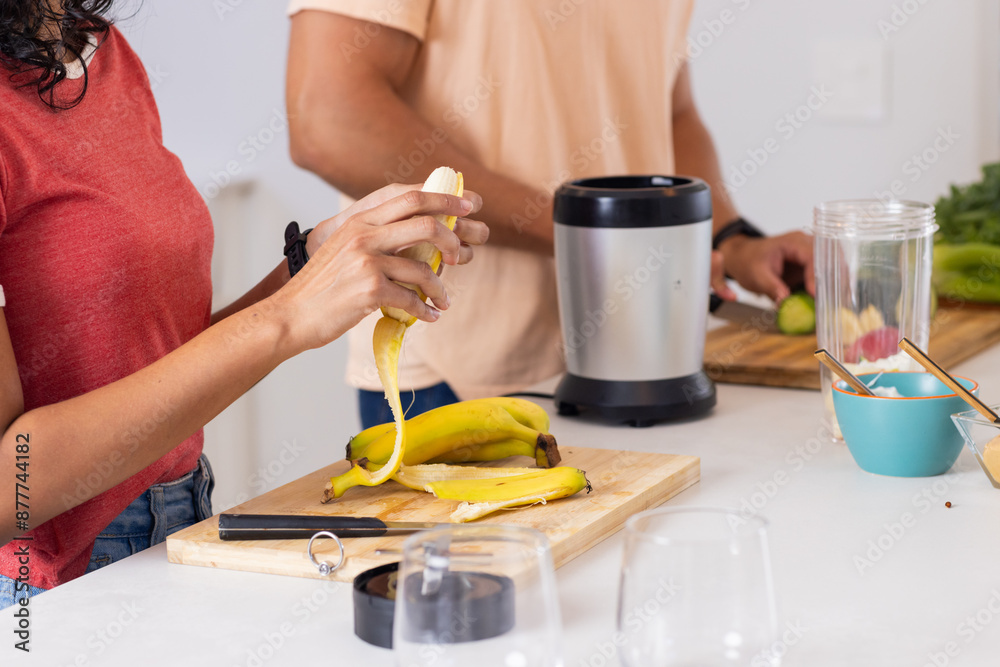 Peeling banana, young couple preparing smoothie in kitchen with blender Peeling banana, young couple preparing smoothie in kitchen with blender