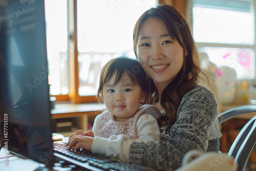 Asian Woman Professional Mom Multitasking with Baby Toddler Child on Lap while Working from Home with Flexible Schedule photo