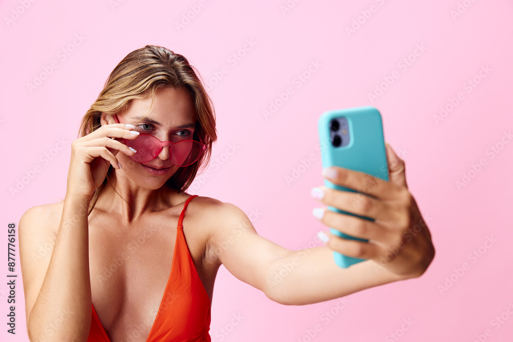 Vibrant woman in bright red swimsuit posing for a selfie on a cheerful pink backdrop Vibrant woman in bright red swimsuit posing for a selfie on a cheerful pink backdrop