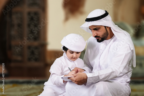 Photography Middle East Arab father parent teaching young son both wearing Kandura inside a traditional home