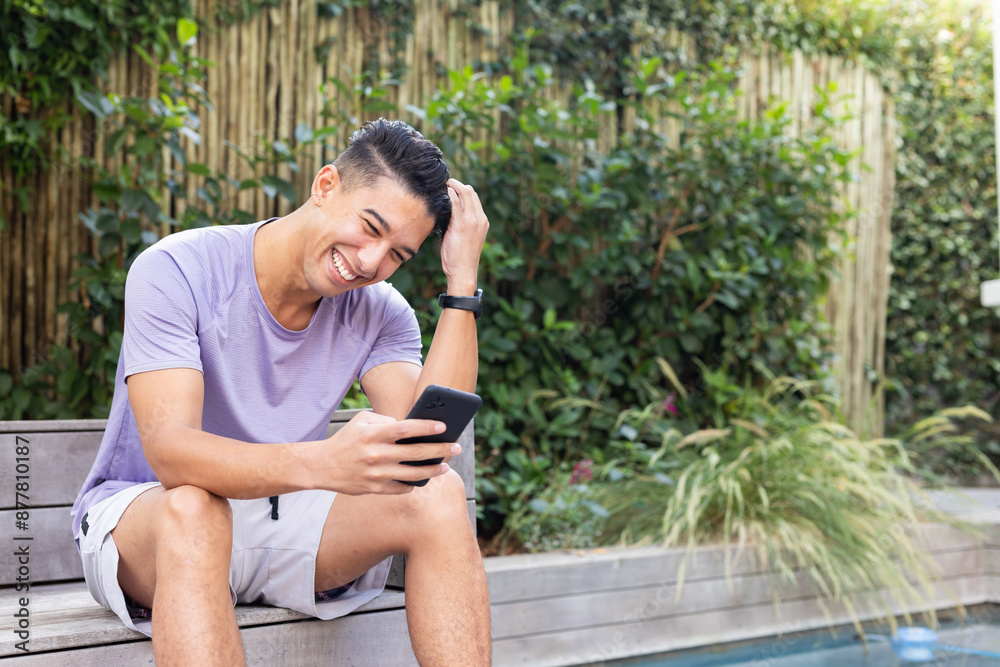 Smiling man sitting by pool, using smartphone and enjoying leisure time, copy space