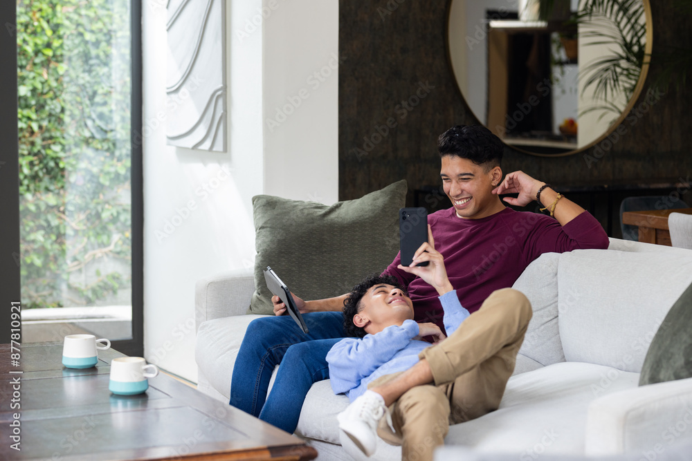 Relaxing on couch, male gay couple using smartphone and tablet at home, copy space Relaxing on couch, male gay couple using smartphone and tablet at home, copy space