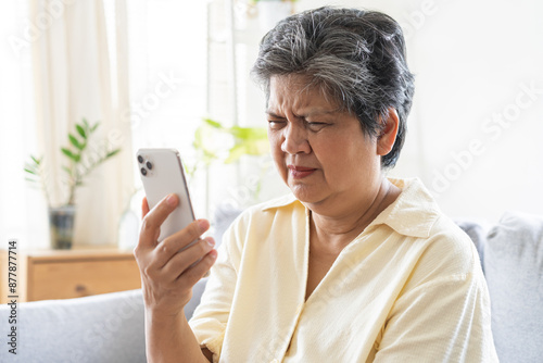 Tableau sur toile Presbyopia, Hyperopia mature, aged asian woman having vision problem trying to stare text on smart mobile phone screen on sofa at home, eye disease of elderly