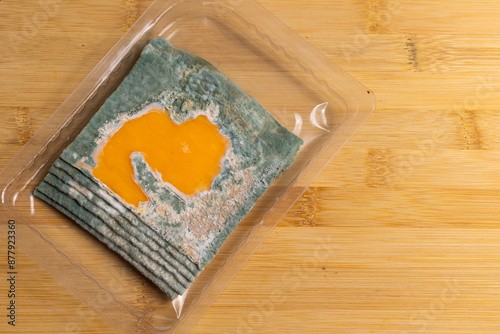 Obraz na płótnie Slices of moldy yellow cheese arranged on a bamboo cutting board. Green mold spores on food. Expired wasted food w salonie