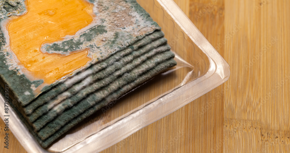 Slices of moldy yellow cheese arranged on a bamboo cutting board. Green mold spores on food. Expired wasted food