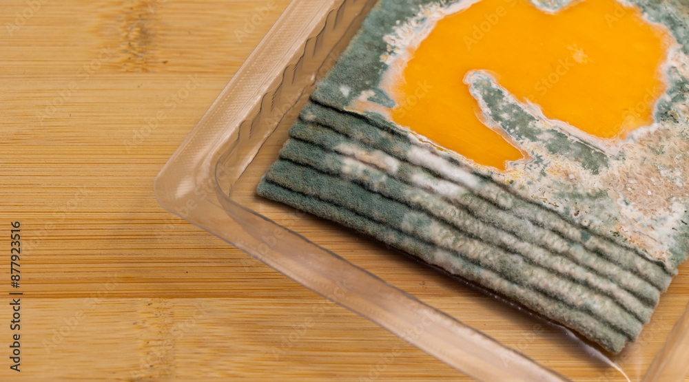 Slices of moldy yellow cheese arranged on a bamboo cutting board. Green mold spores on food. Expired wasted food