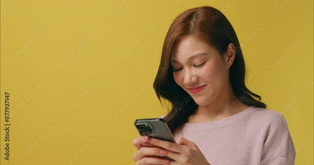 Young woman looks excited and happy when she receives some message from her mobile phone. Isolated on yellow background in studio. Young woman looks excited and happy when she receives some message from her mobile phone. Isolated on yellow background in studio.