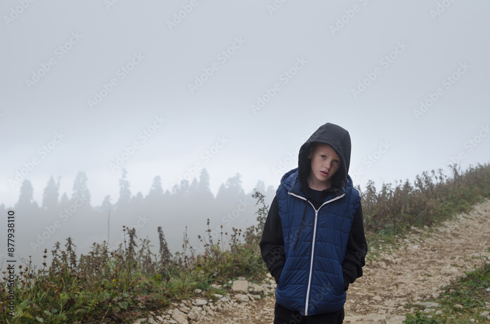 A boy on a mountain stands at the edge, looking into the distance A boy on a mountain stands at the edge, looking into the distance