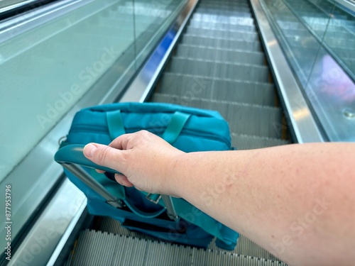 Hand and arm pulling teal suitcase on an escalator at CVG airport photo