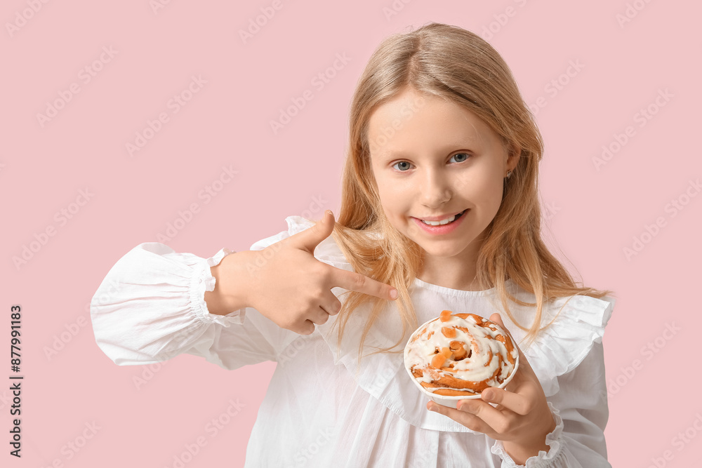 Cute little girl pointing at tasty cinnamon bun on color background Cute little girl pointing at tasty cinnamon bun on color background
