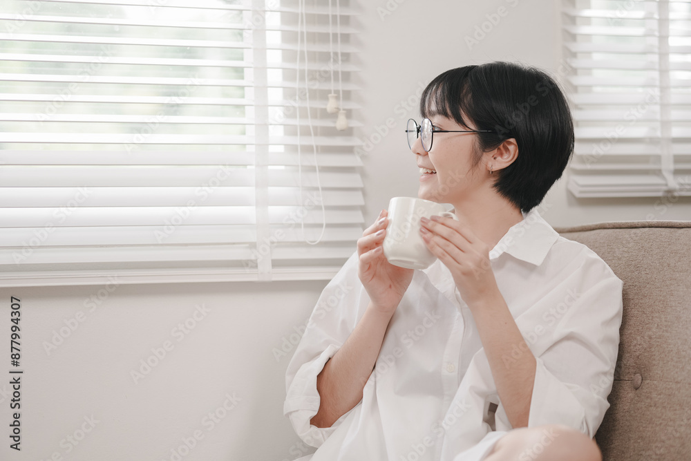 A woman is sitting in a chair with a white shirt on and a cup in her hand. She is smiling and she is enjoying her coffee A woman is sitting in a chair with a white shirt on and a cup in her hand. She is smiling and she is enjoying her coffee