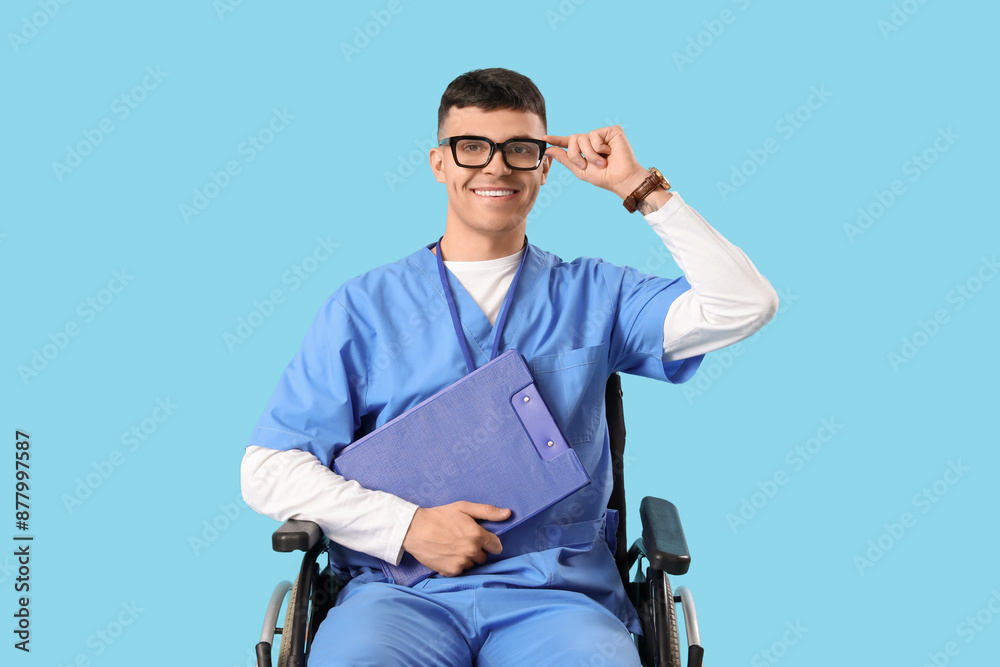 Young male doctor in wheelchair with clipboard on blue background Young male doctor in wheelchair with clipboard on blue background