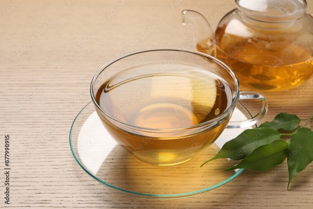 Refreshing green tea in cup, leaves and teapot on wooden table, closeup Refreshing green tea in cup, leaves and teapot on wooden table, closeup