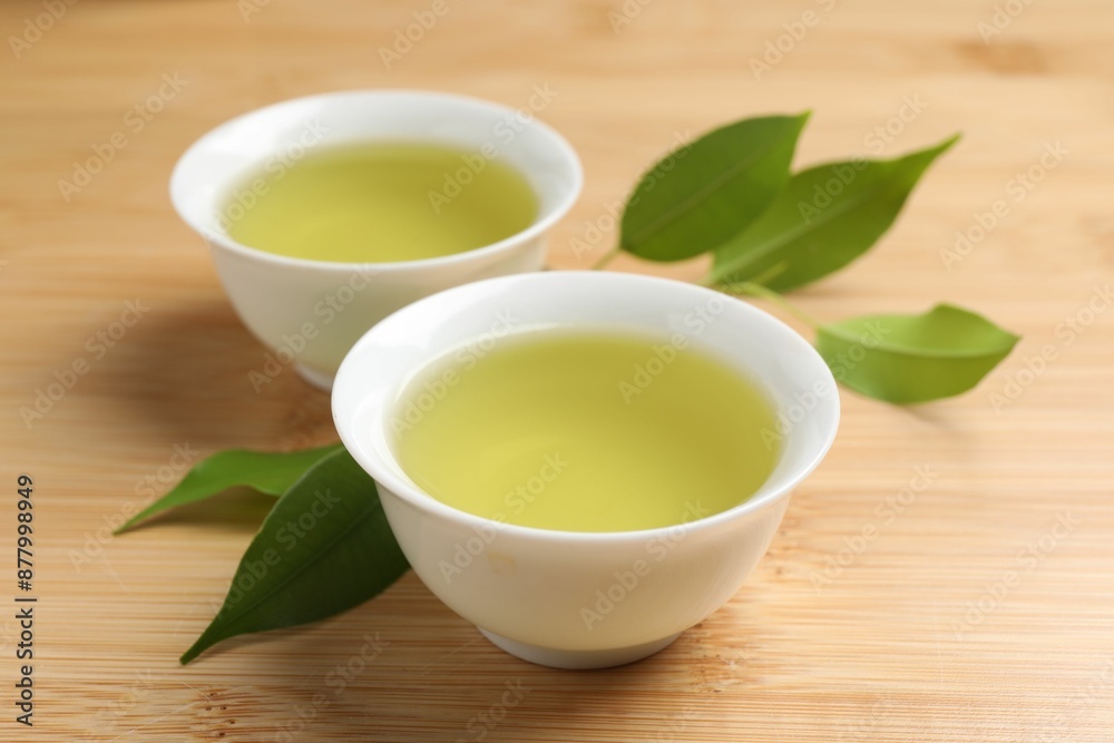 Refreshing green tea in cups and leaves on wooden table, closeup