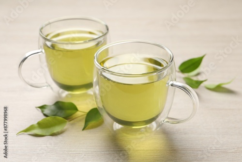 Refreshing green tea in cups and leaves on wooden table, closeup
