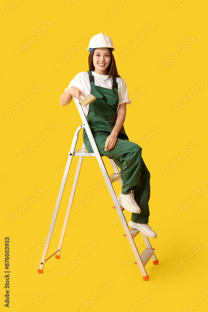Young female painter with brush sitting on ladder against yellow background Young female painter with brush sitting on ladder against yellow background