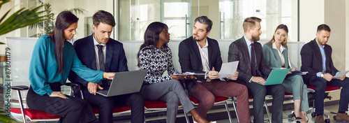 Tableau sur toile Young diverse business people sitting on chairs in a row with resumes and laptops in hands chatting and talking with each other