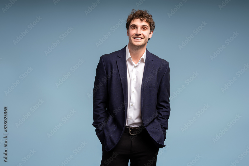 Confident young businessman smiling with hands in pockets on blue background looking at camera Confident young businessman smiling with hands in pockets on blue background looking at camera