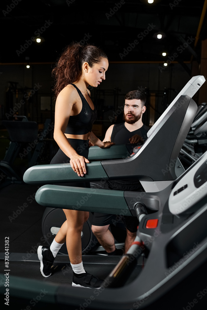 A male personal trainer and a brunette sportswoman are energetically running on a treadmill in a gym.