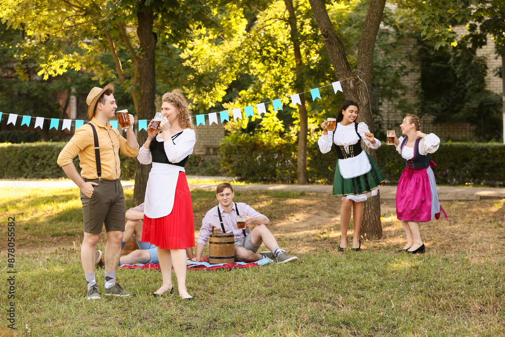 Fototapeta premium Young couple in traditional German clothes drinking beer outdoors. Octoberfest celebration