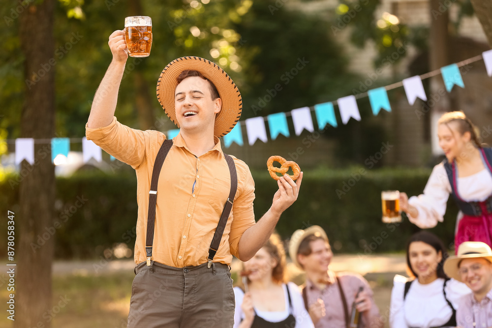 Fototapeta premium Young man in traditional German clothes with beer and pretzel celebrating Octoberfest outdoors