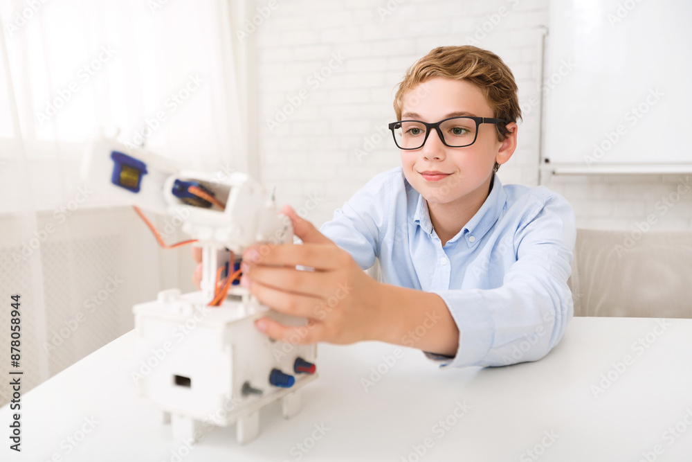 A young boy sits at a desk in a classroom, focusing intently as he assembles a robotic arm kit. The focus on his face suggests his interest in STEM education and the excitement of creating A young boy sits at a desk in a classroom, focusing intently as he assembles a robotic arm kit. The focus on his face suggests his interest in STEM education and the excitement of creating