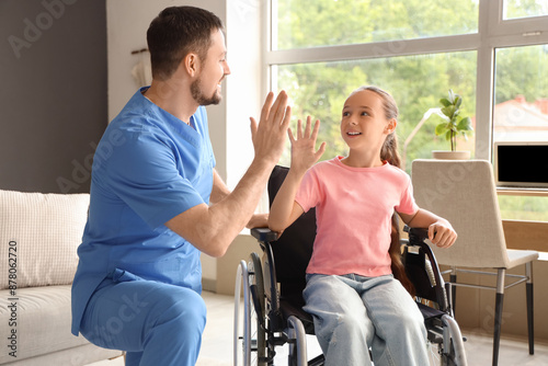 Little girl in wheelchair with nurse giving each other high-five at home