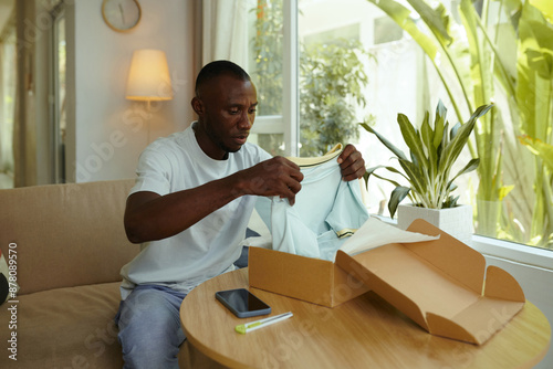 Quadro em tela Upset man unpacking box and getting T-shirt of small size while sitting in the r