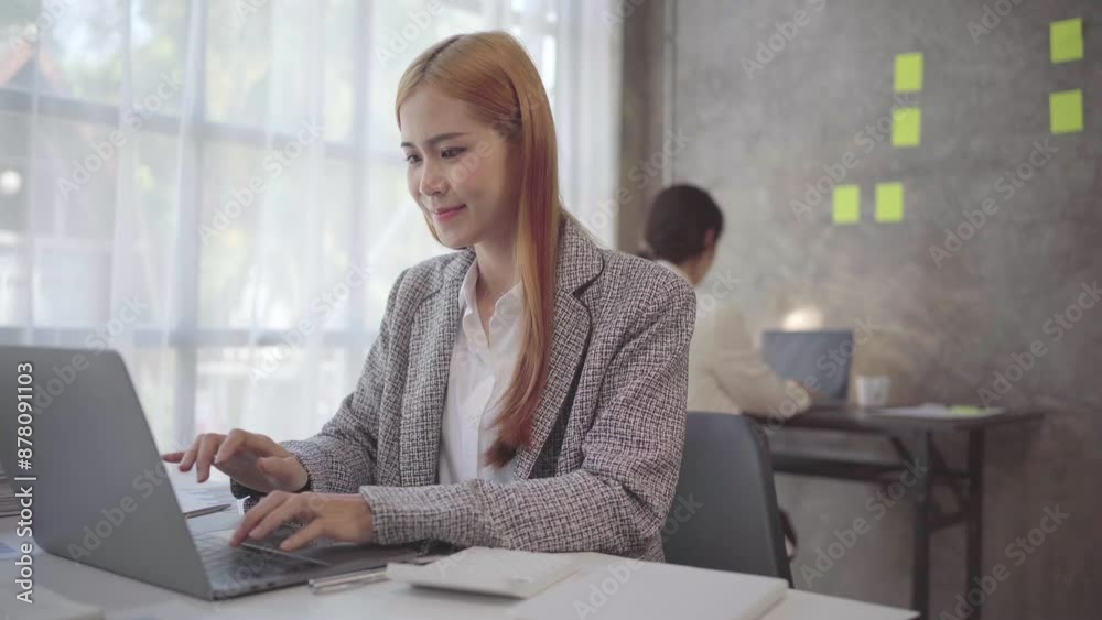 Focused businesswoman typing on laptop in modern office with colleague working in background. Professional, engaged, and productive in corporate environment Focused businesswoman typing on laptop in modern office with colleague working in background. Professional, engaged, and productive in corporate environment