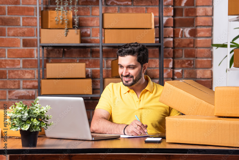 Indian asian Man Using Laptop and Smartphone to Manage and Ship Online Orders from Warehouse Indian asian Man Using Laptop and Smartphone to Manage and Ship Online Orders from Warehouse
