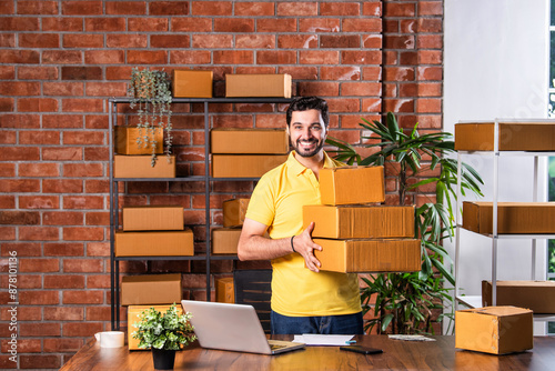 Indian asian Man Using Laptop and Smartphone to Manage and Ship Online Orders from Warehouse photo