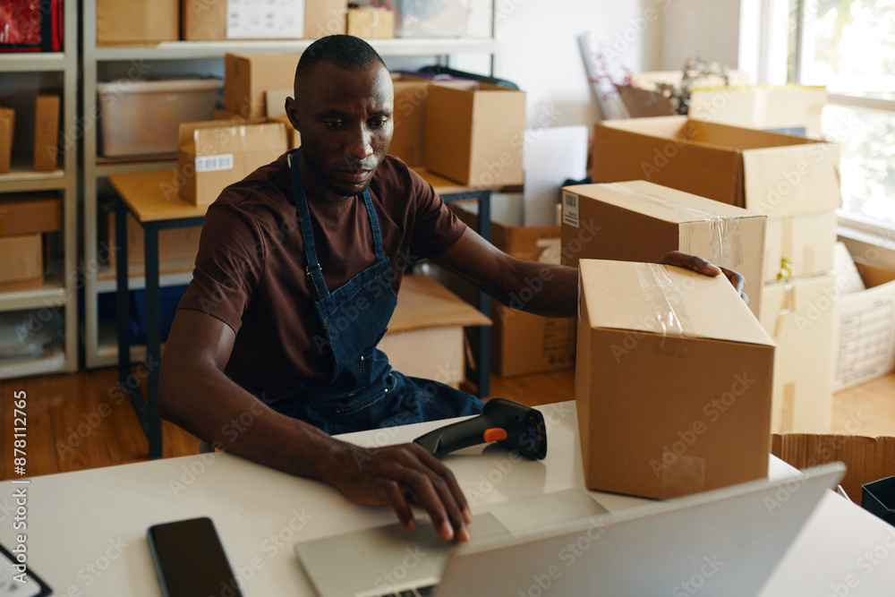 African American man entering data of parcels in laptop while working in warehouse African American man entering data of parcels in laptop while working in warehouse