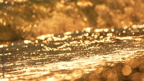 Golden sunset on the beach. Foamy waves rolling towards golden sand beach under low warm sun light. Slow motion. Nobody. Holiday recreation concept. Abstract nautical summer ocean sunset nature.
