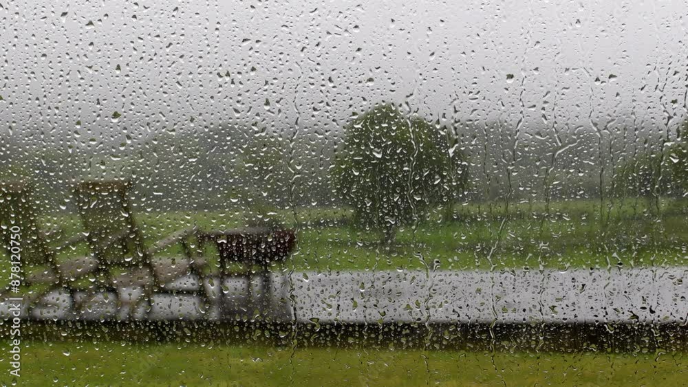 Heavy rain with raindrops running down a window looking out to softly focused garden. Selective focus on the rain drops. English weather and stormy scene