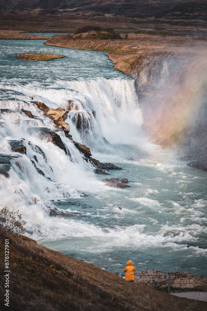 Stunning view of the Gullfoss waterfall with a tourist wearing a yellow jacket. Gullfoss is the most popular waterfall in Iceland and one of its most iconic sights.