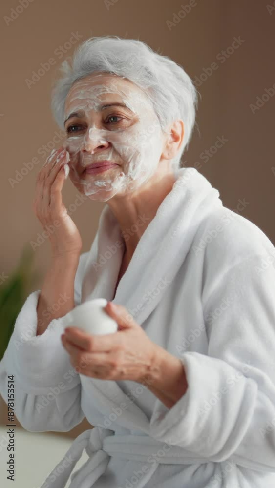 Rejuvenating face mask for aging skin, old lady applying cream on skin, vertical portrait. Senior woman using moisturizing anti-ageing cream, beauty treatment for stay young in old age, better aging