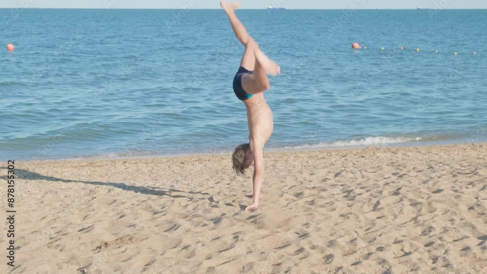 boy makes an acrobatic element on sandy beach of sea, performs gymnastic exercises with her head upside down
boy makes an acrobatic element on sandy beach of sea, performs gymnastic exercises with her head upside down