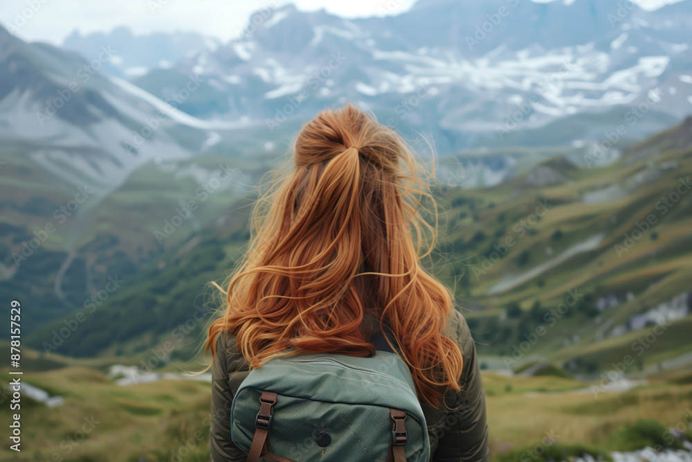 Red-haired girl with a backpack against the backdrop of mountains. View from the back of a girl in the mountains Red-haired girl with a backpack against the backdrop of mountains. View from the back of a girl in the mountains