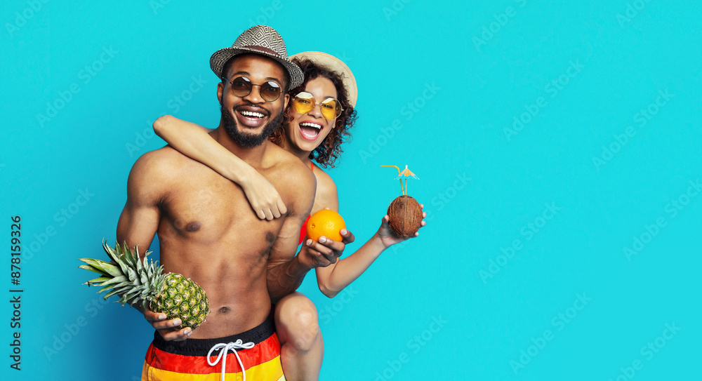 African American young couple posing playfully against a blue backdrop, enjoying a tropical theme. They are both smiling and seem to be having a great time, copy space African American young couple posing playfully against a blue backdrop, enjoying a tropical theme. They are both smiling and seem to be having a great time, copy space
