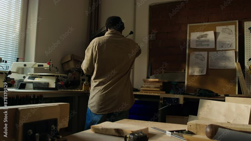 Back view of professional male carpenter standing in woodworking workshop and using drill press machine Back view of professional male carpenter standing in woodworking workshop and using drill press machine